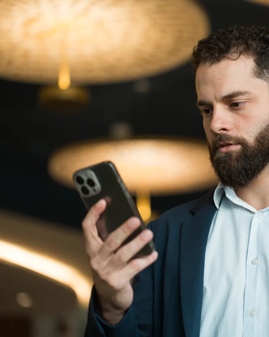 Philip Brás concentrado olhando o celular, em ambiente de luz baixa